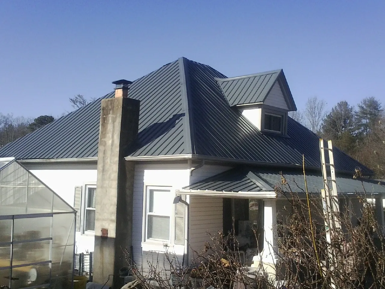 Dark blue standing seam metal roof on a white farmhouse with dormer — Slate & Tile Roof Repair by Roofing Brothers in Franklinton