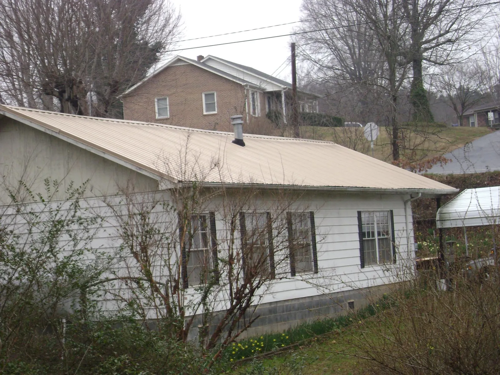 Tan metal roof on a white sided house set into a hillside — Commercial Roofing by Roofing Brothers in Franklinton