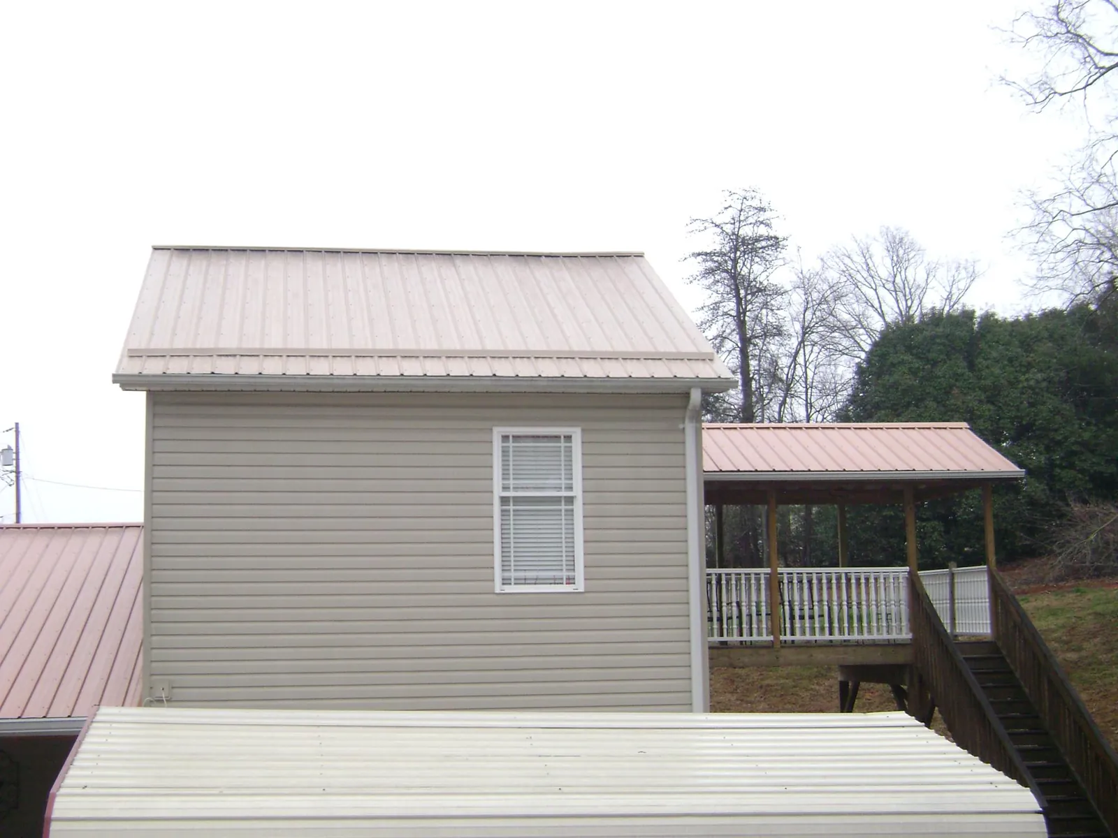 Tan metal roofs on a two story addition and attached porch, from a Roof Replacement job in Franklinton